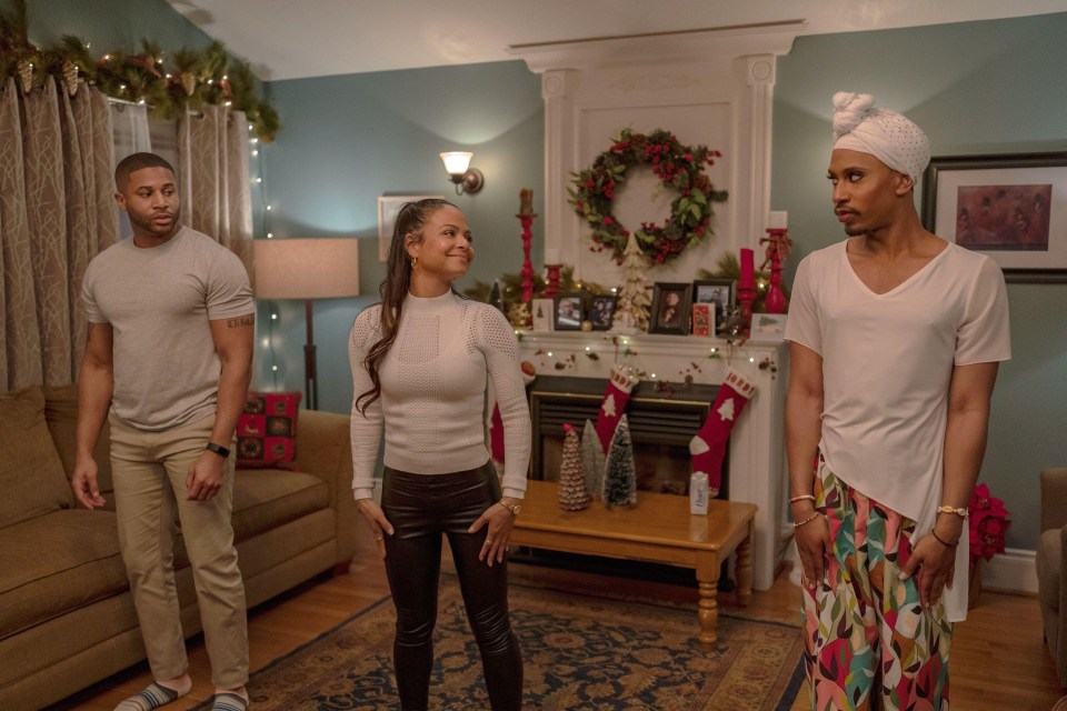 three people standing in a living room with christmas stockings on the mantle