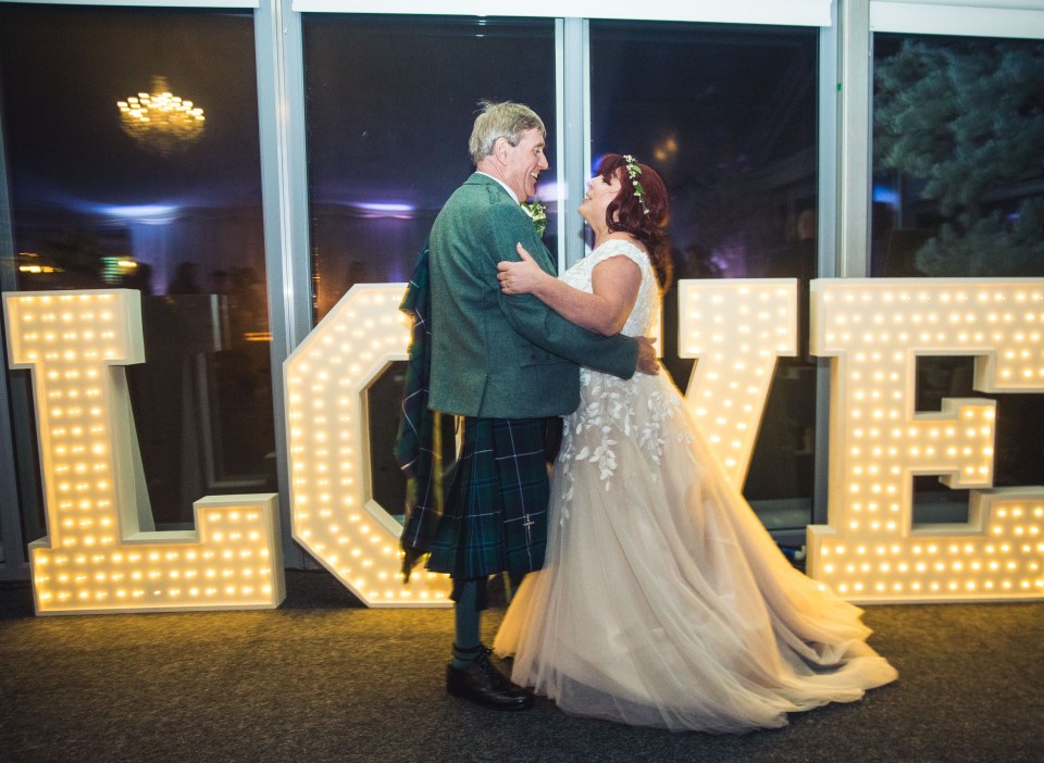 a bride and groom are dancing in front of a large love sign