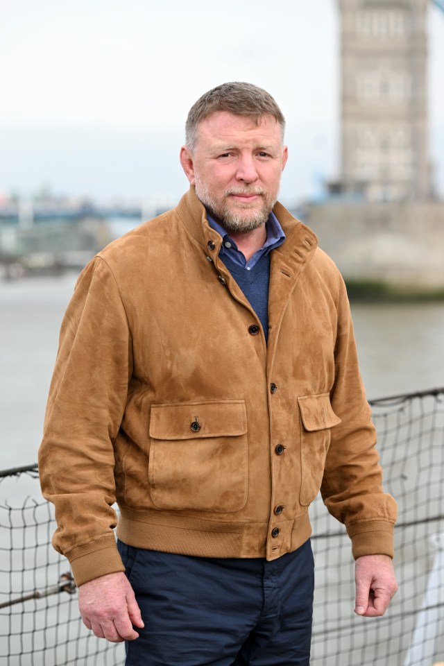 a man in a brown jacket stands in front of a fence