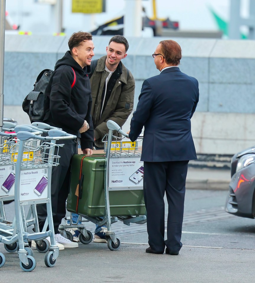 a man in a suit talks to two men carrying luggage