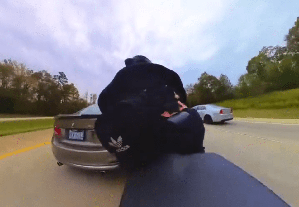 a man wearing a black adidas jacket is standing in front of a bmw