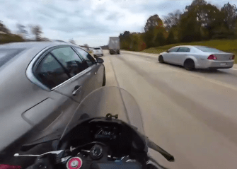 a car and a motorcycle are driving down a highway and the motorcycle 's speedometer reads 104