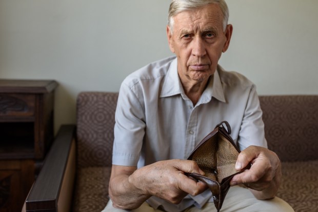 an elderly man sitting on a couch holding an empty wallet