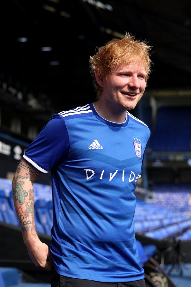 Ed Sheeran at a soccer match wearing an Ipswich Town jersey.