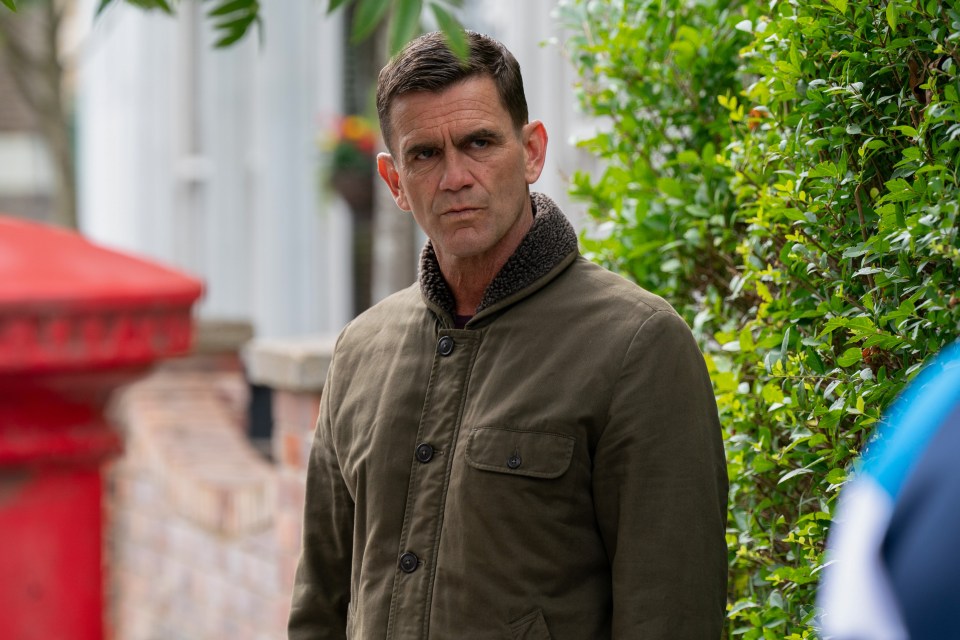 a man in a green jacket stands in front of a red mailbox