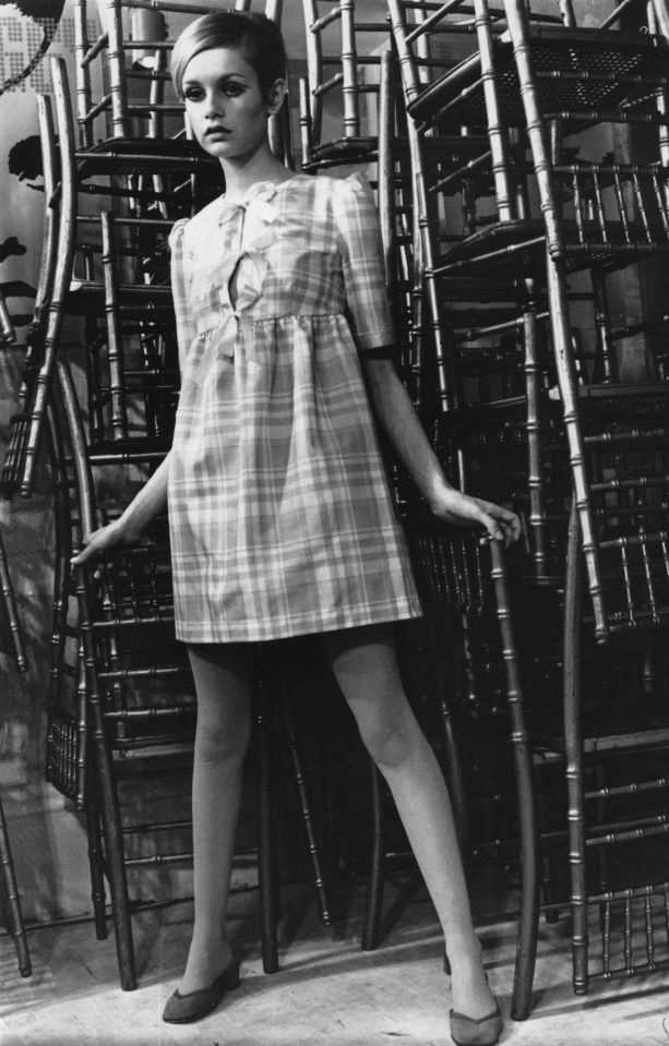 a woman in a plaid dress stands in front of a stack of chairs