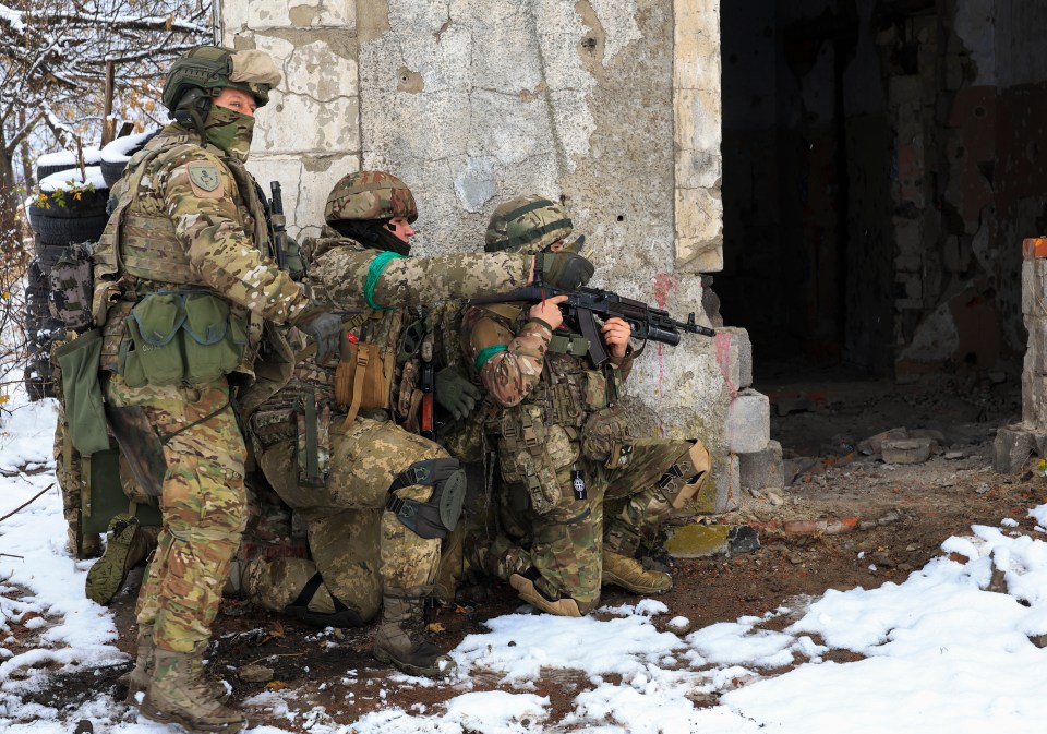 a group of soldiers are kneeling down in the snow and one of them has the letter t on his chest