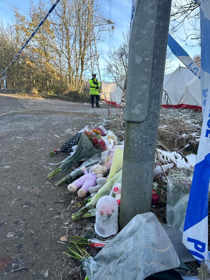 a police officer stands behind a pile of flowers and teddy bears