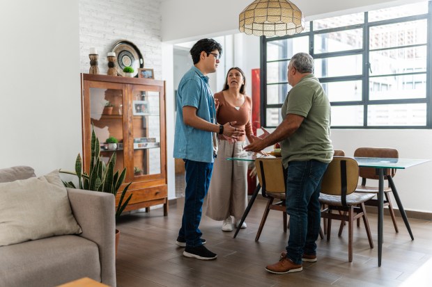 a group of people standing in a living room talking to each other