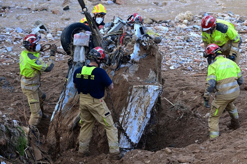 Firefighters use a crane to dig up the wreckage of a car in search of victims buried on a riverbank in Paiporta, in the region of Valencia, eastern Spain