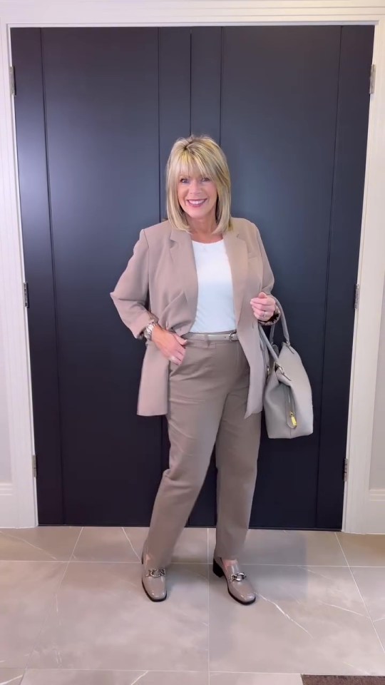 a woman standing in front of a black door wearing a tan suit