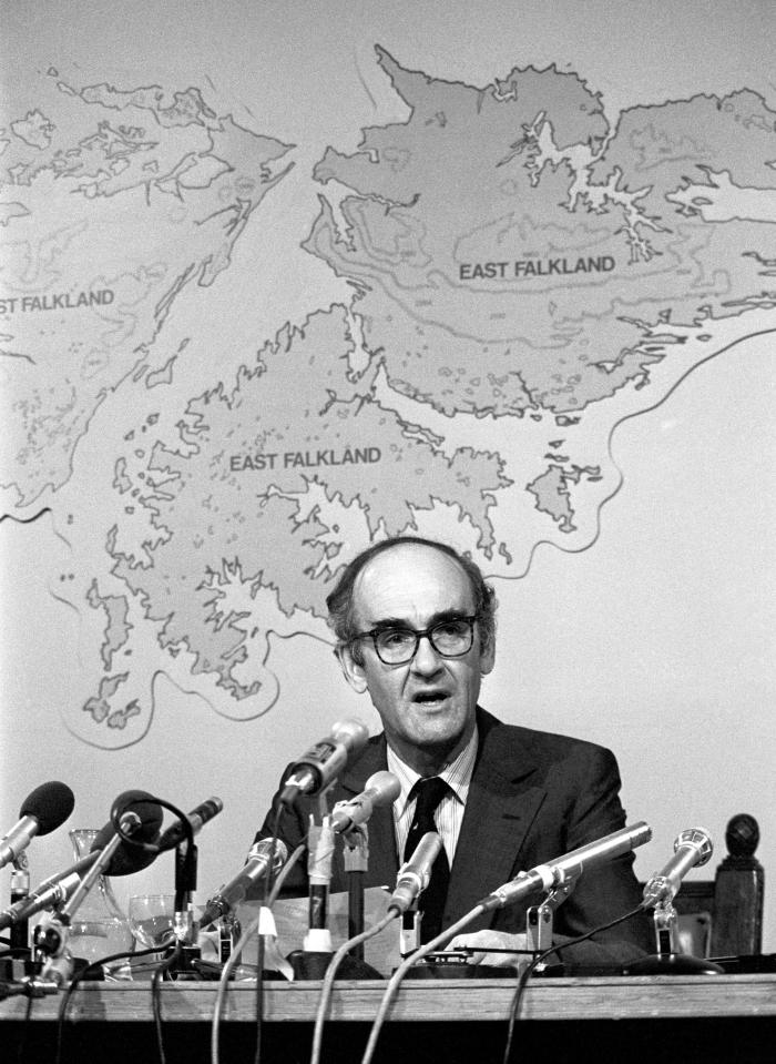 a man sitting at a table with microphones in front of a map that says east falkland