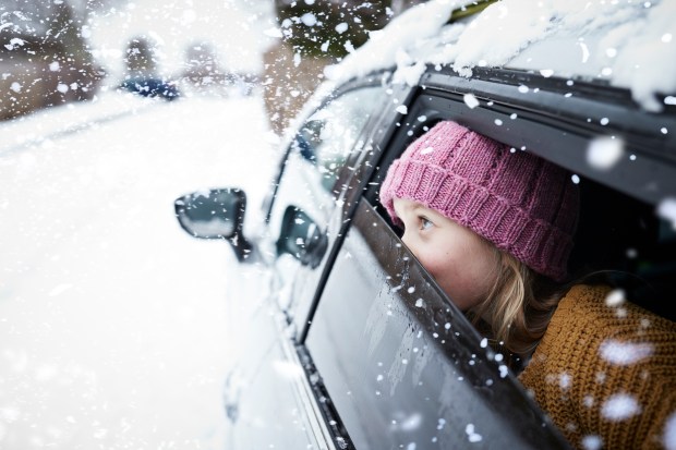 a girl wearing a pink hat looks out of a car window in the snow