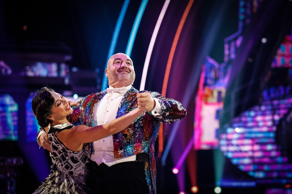 a man in a sequined jacket is dancing with a woman