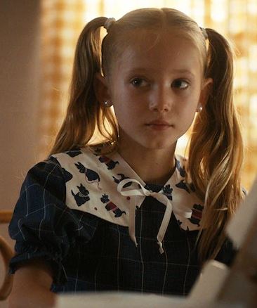 a little girl wearing pigtails and a collar is sitting at a table .