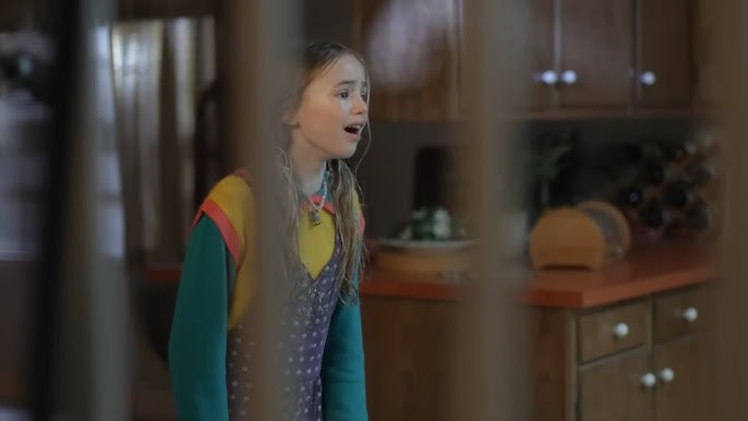 a young girl is standing in a kitchen behind a fence .