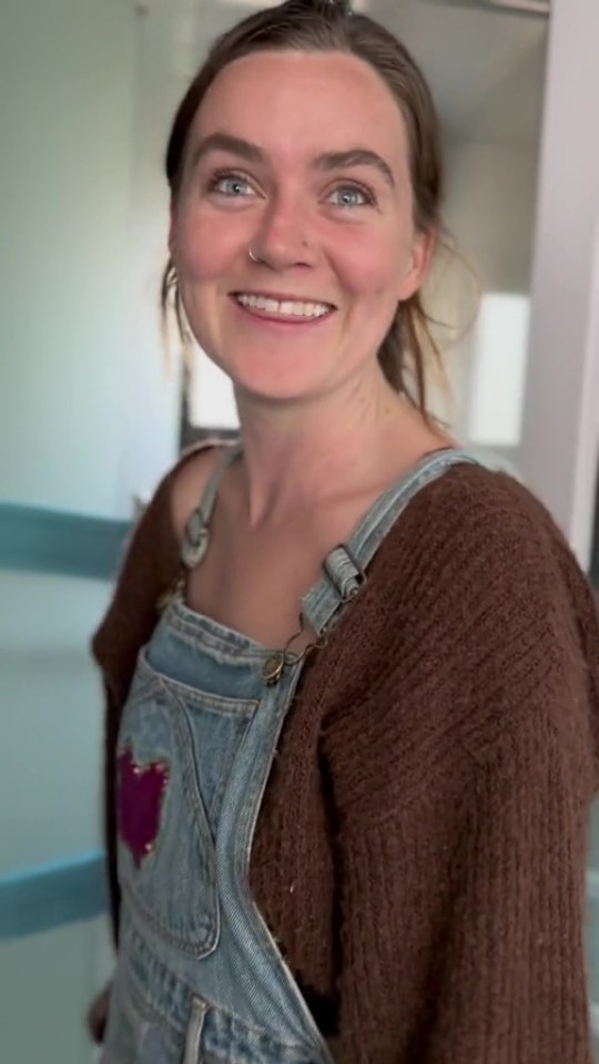 a woman wearing overalls and a brown sweater smiles for the camera