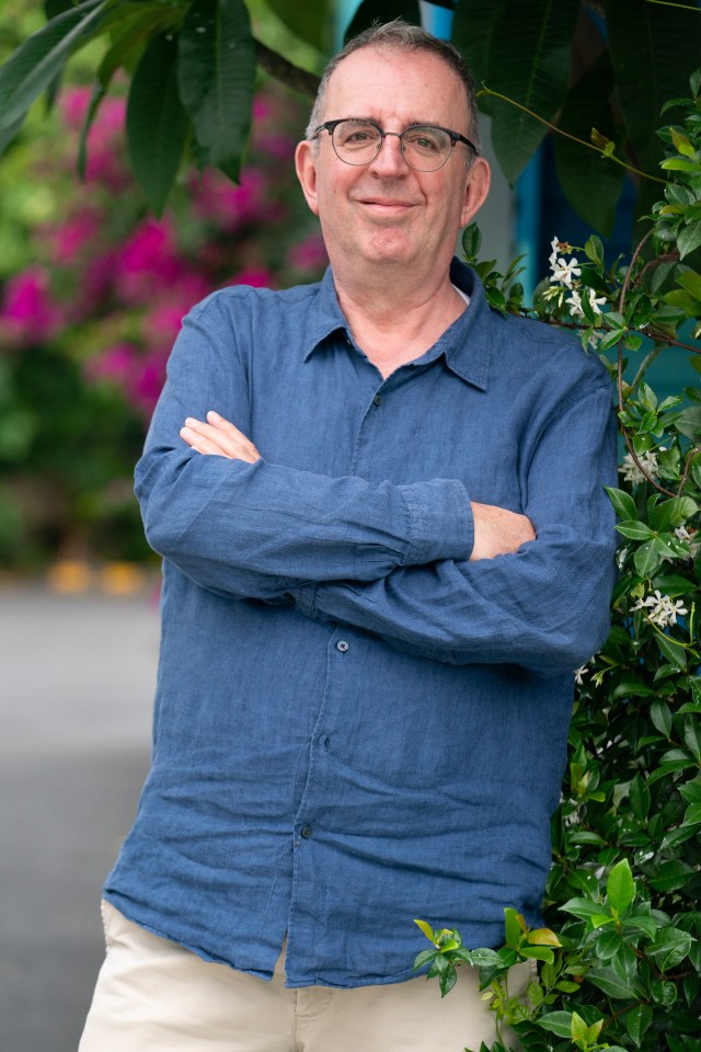 a man wearing glasses and a blue shirt stands with his arms crossed