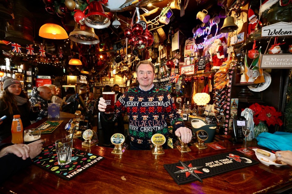 Man in Christmas sweater holding a pint at a pub.