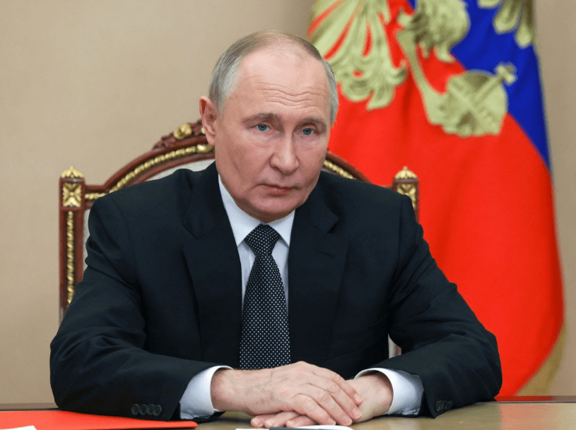 a man in a suit and tie sits in front of a russian flag