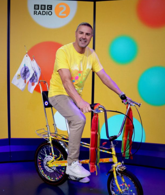 a man is riding a yellow bicycle in front of a sign that says bbc radio 2