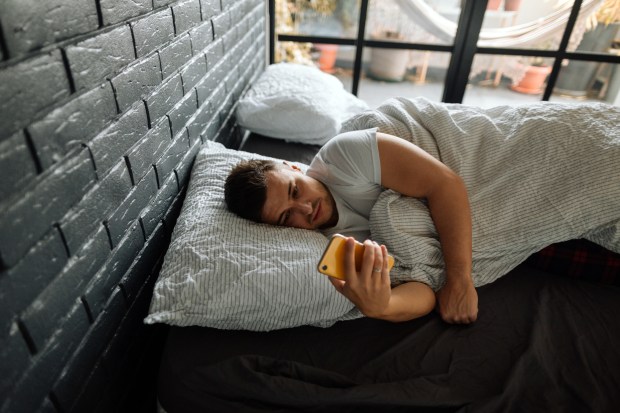 a man laying in bed looking at his phone