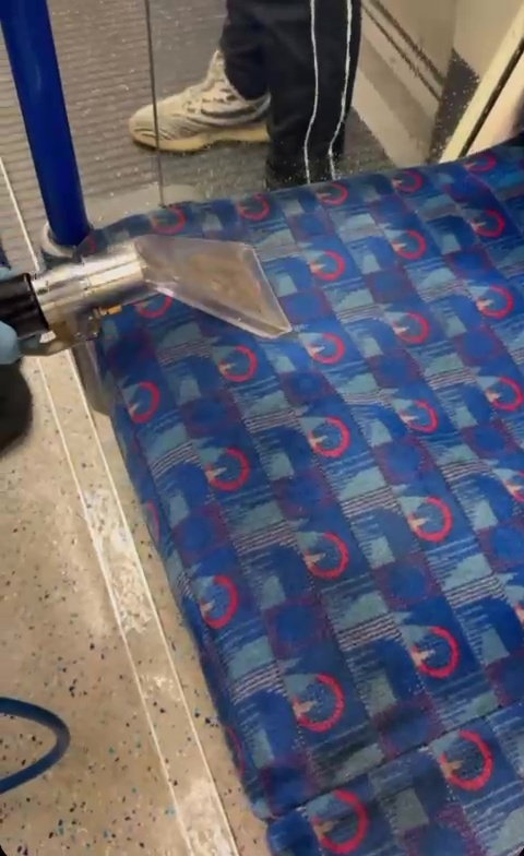 a person is cleaning a blue seat on a train with a vacuum cleaner .