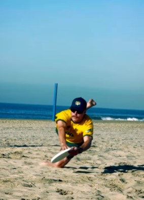 a man in a yellow shirt is playing frisbee on the beach