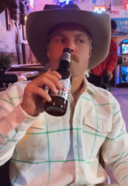 a man in a cowboy hat is drinking a coors light beer