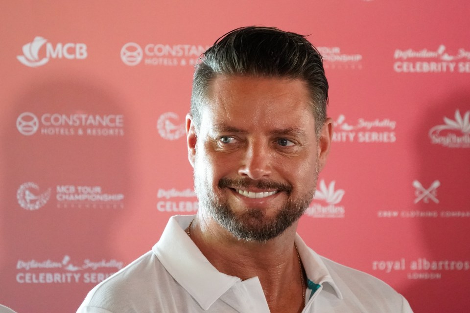 a man with a beard is smiling in front of a pink background that says mcb