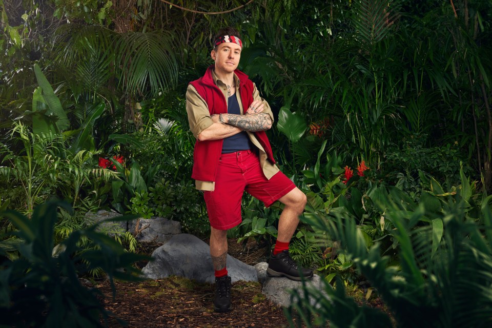 a man in a red vest is standing in the jungle