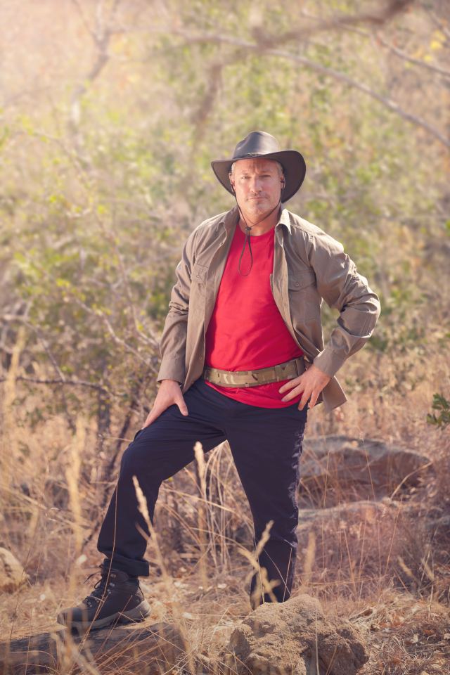 a man wearing a cowboy hat and a red shirt is standing on a rock