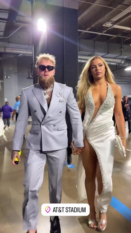 a man in a suit and a woman in a white dress walk through an at & t stadium parking garage