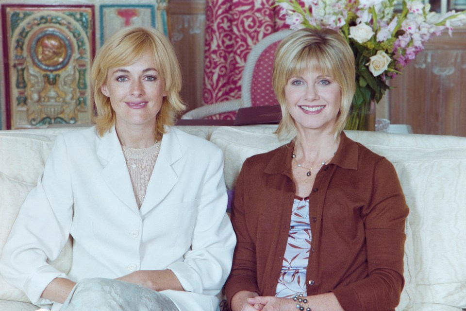 two women sit next to each other on a couch and smile for the camera