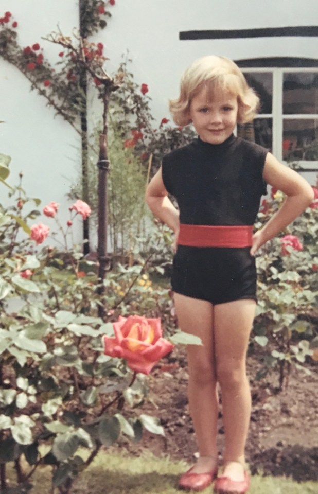 a little girl in a black and red outfit stands in front of roses