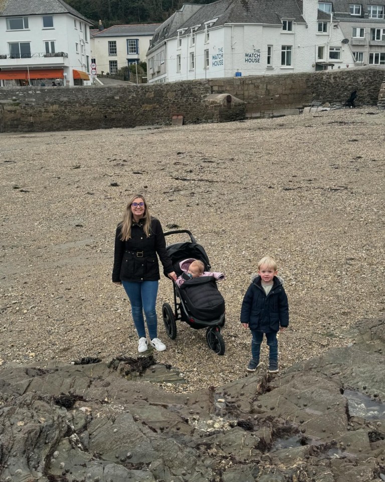 a woman pushes a stroller on a beach in front of a building that says the watch house