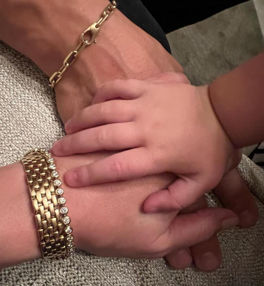 a woman wearing a gold bracelet holds a baby 's hand