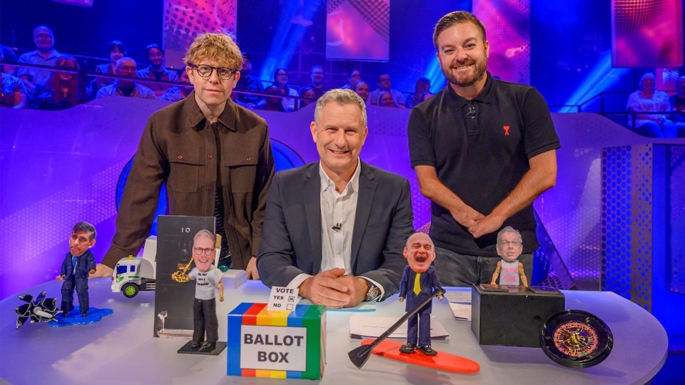 three men sit at a table with a ballot box in front of them