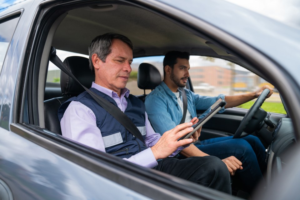 Driving instructor using a tablet while grading a man’s driving test – learning to drive concepts