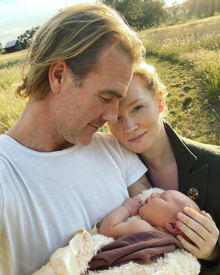 a man and woman holding a baby in a field