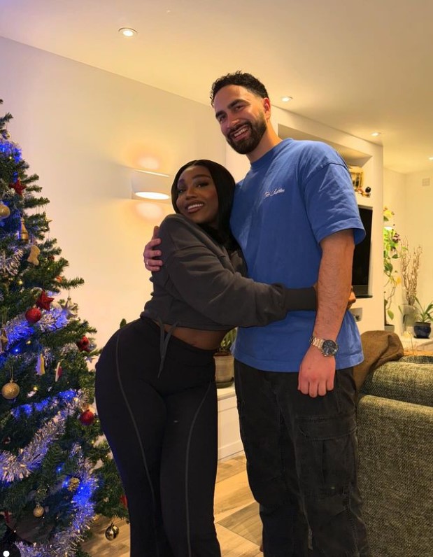 a man in a blue columbia shirt is hugging a woman in front of a christmas tree