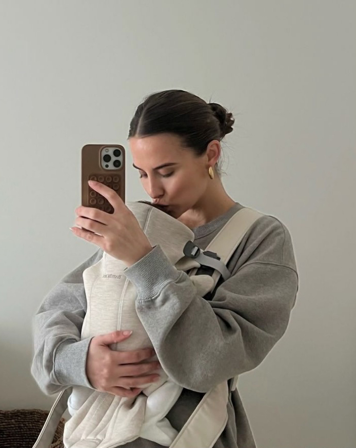 a woman is holding a baby in a carrier and taking a selfie