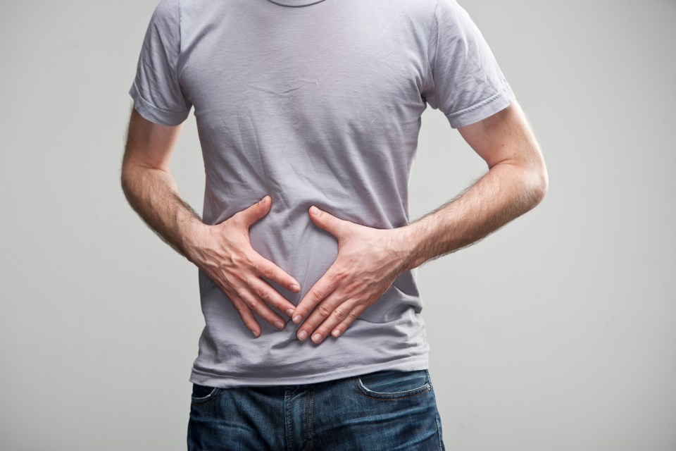 a man in a grey shirt holds his hands on his stomach