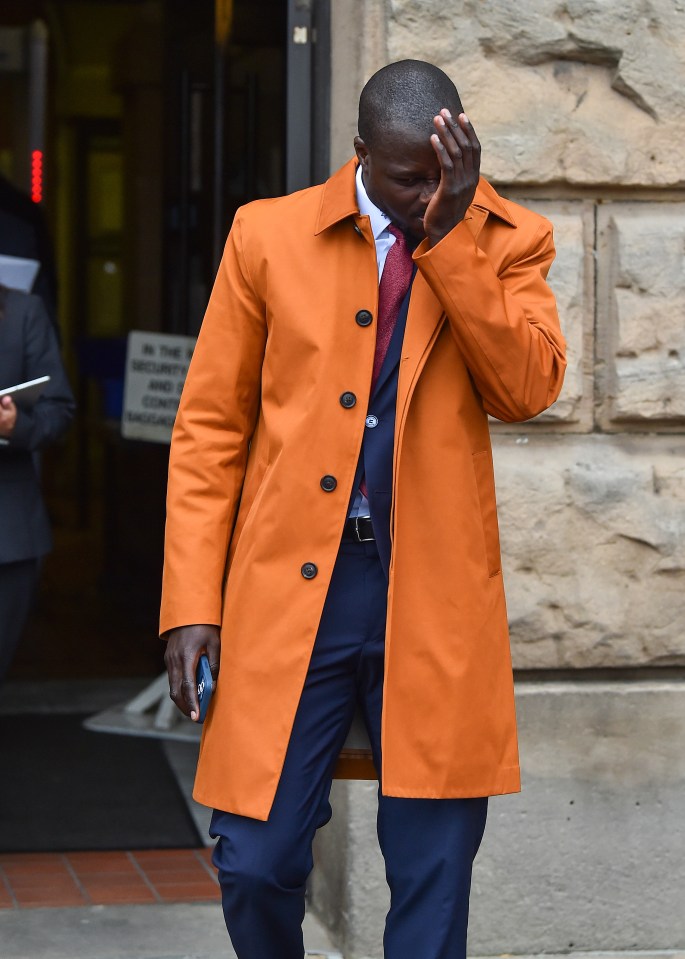 a man in an orange coat covering his face with his hand