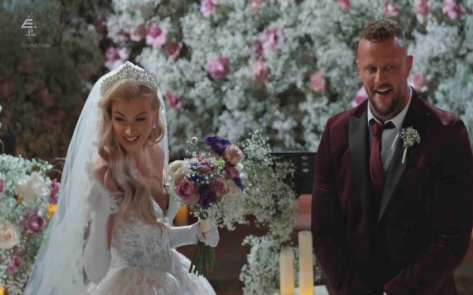 a bride and groom standing in front of a wall of flowers