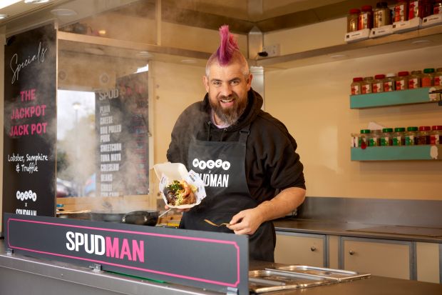 a man with a mohawk stands behind a sign that says spudman