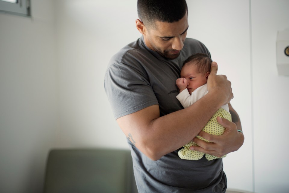 a man in a grey shirt holds a baby in his arms