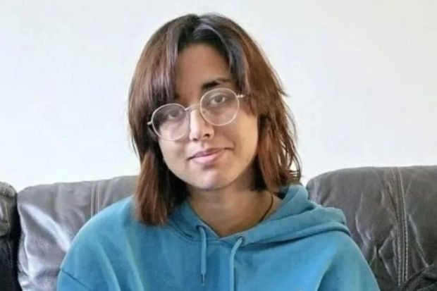 a woman wearing glasses and a blue hoodie is sitting on a couch .