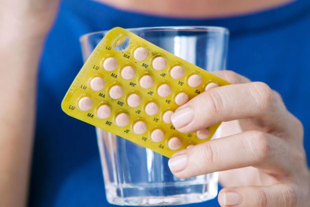 a woman is holding a blister pack of pills and a glass of water