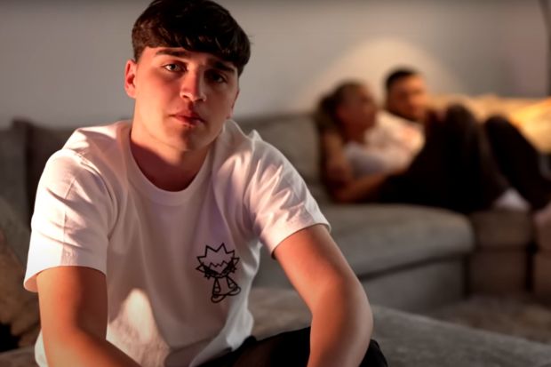 a young man wearing a white t-shirt with a cat on it sits on a couch